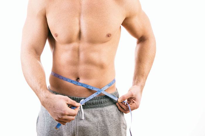 Un homme musclé prend ses mensurations après avoir utilisé une ceinture avec electrostimulation